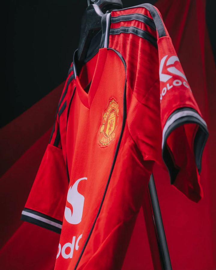 Striker Store Manchester United 2025-26 home jersey in red with black and white detailing hanging on a rack