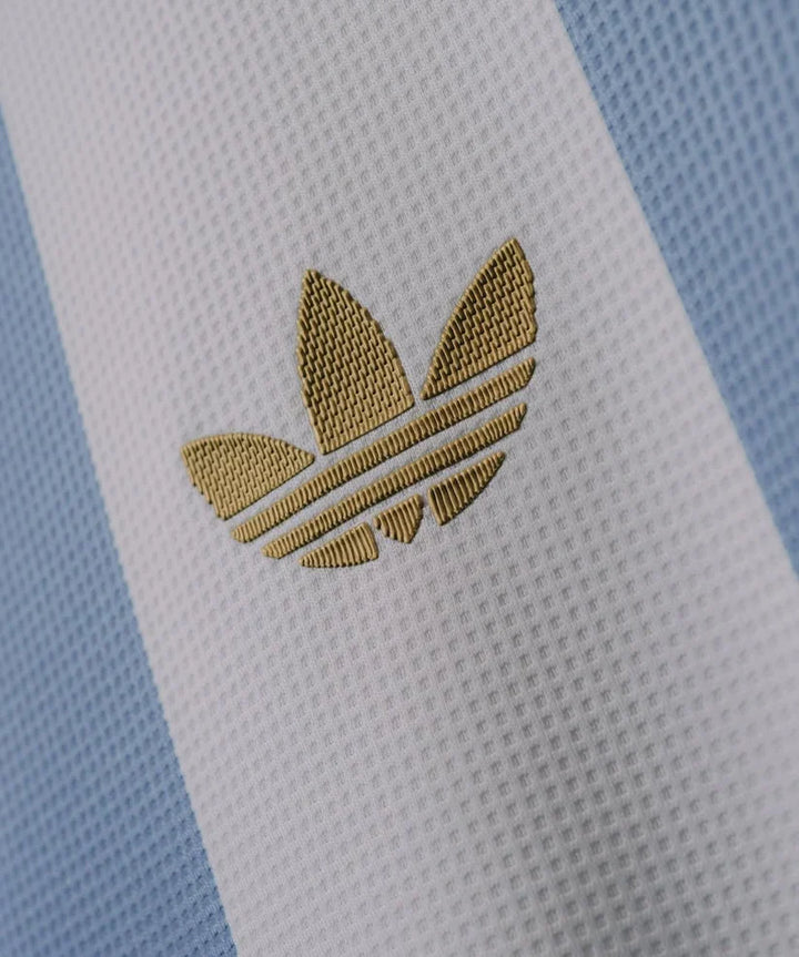 Close-up of the gold Adidas logo on the Argentina anniversary jersey featuring light blue stripes