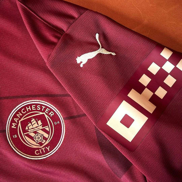 Close-up of Manchester City 2024 third jersey featuring logo and Puma branding in a rich maroon color