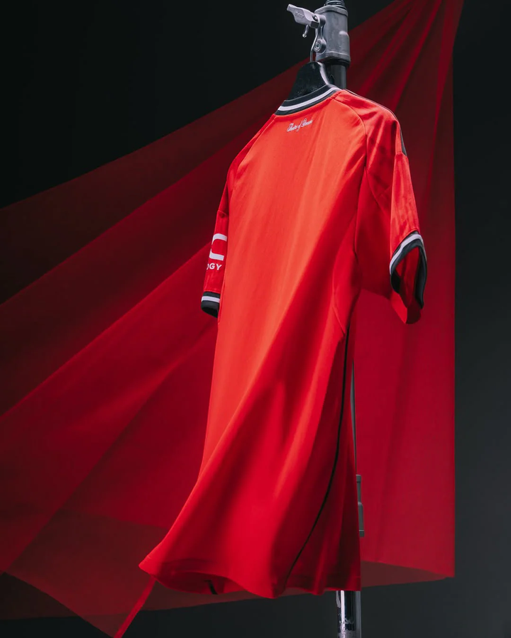Manchester United 2025-26 home jersey in red hanging on a black hanger against red and black background