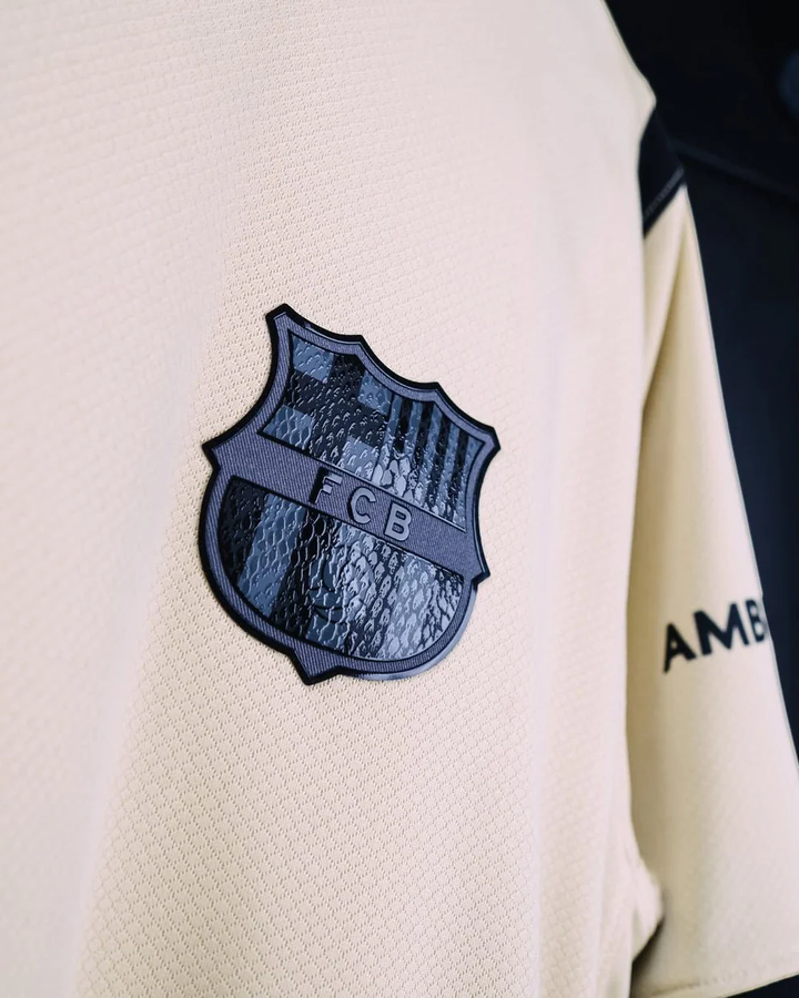 Striker Store Barcelona away jersey 2025-26 cream close up with black embossed FCB crest and textured fabric