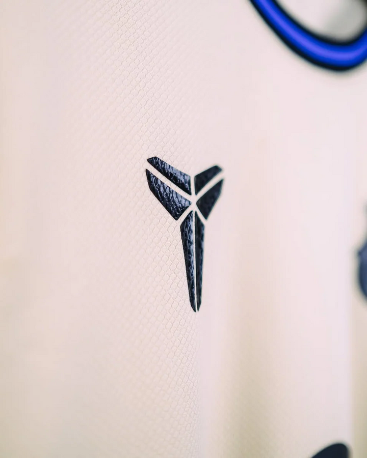 Striker Store Barcelona away jersey 2025-26 close up of textured black emblem on cream fabric with blue trim