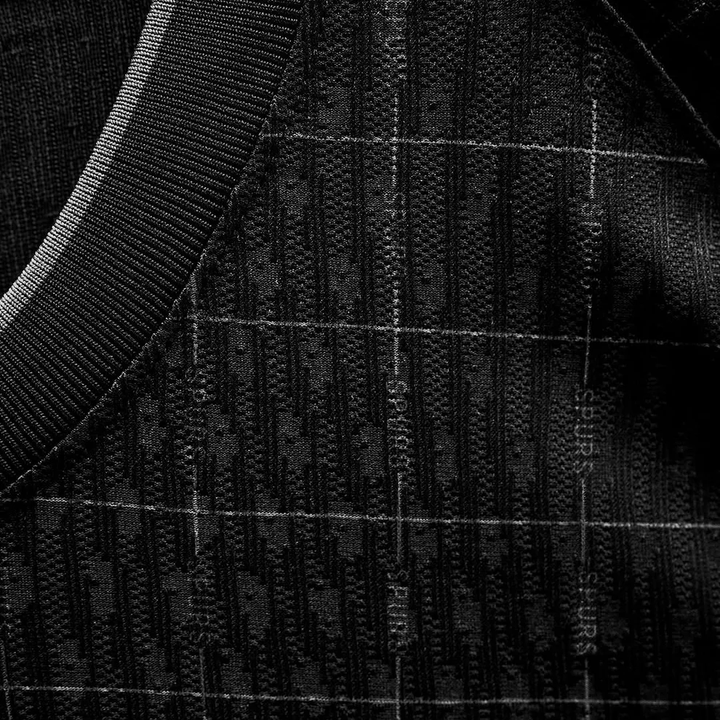 Striker Store close up of Tottenham Hotspur away jersey 2025-26 black textured fabric with subtle grid pattern and ribbed collar