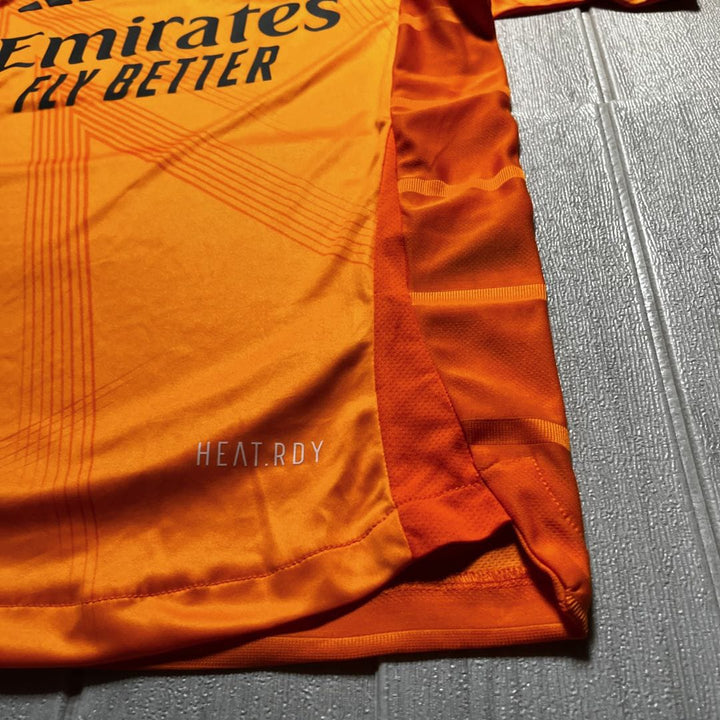 Real Madrid away jersey 2024-25 in bright orange featuring Emirates branding and moisture-wicking technology
